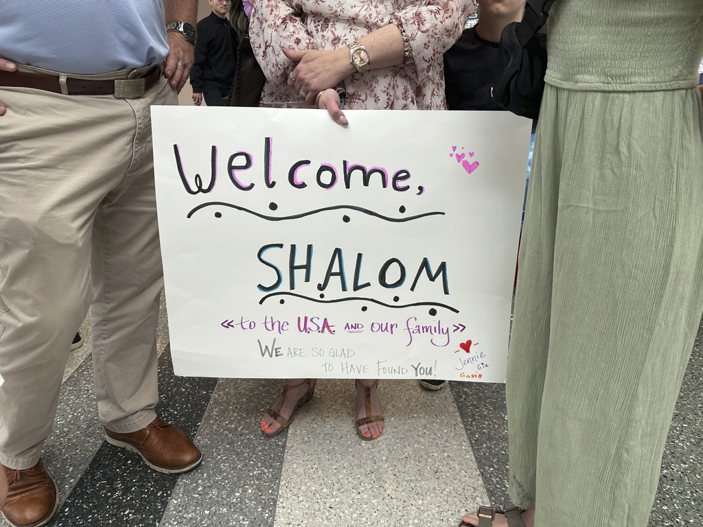 A family member holds up a sign as they meet Shalom Koray for the first time 