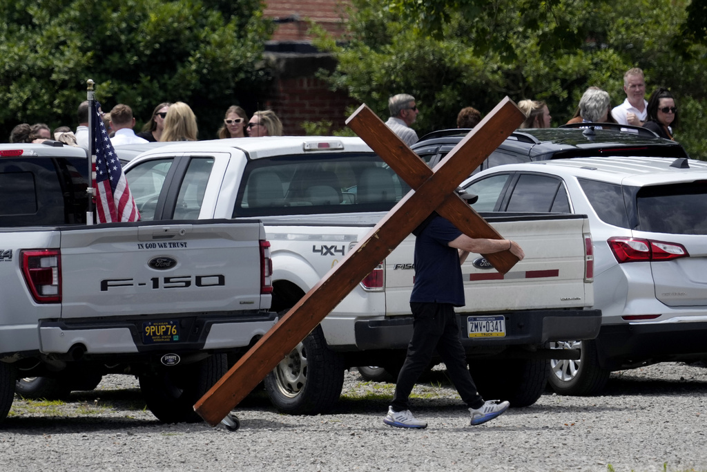 Dan Beazley carries a cross past a line of guests at a visitation for Corey Comperatore at Laube Hall