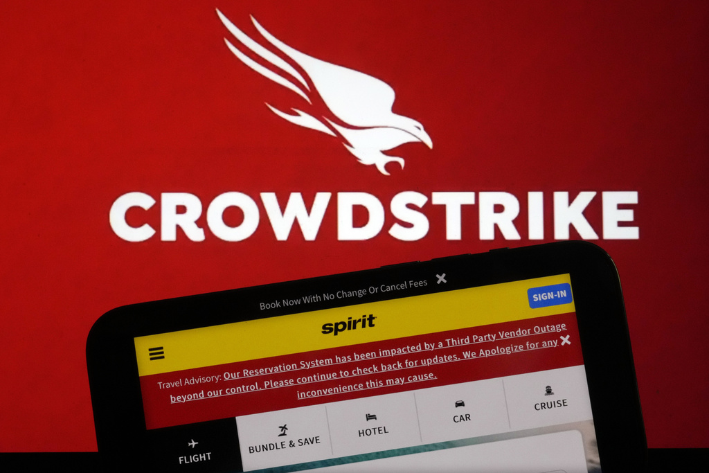 The logo for CrowdStrike and a Spirit Airlines webpage with a Travel Advisory about a third Party Outage impacting their Reservation System are shown on a computer screen and mobile phone screen, in New York