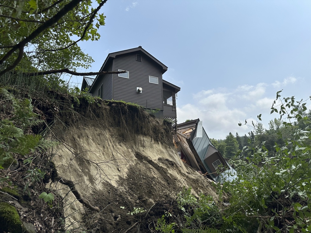 A damaged house sits on a ledge after flooding in Lyndonville, Vt.