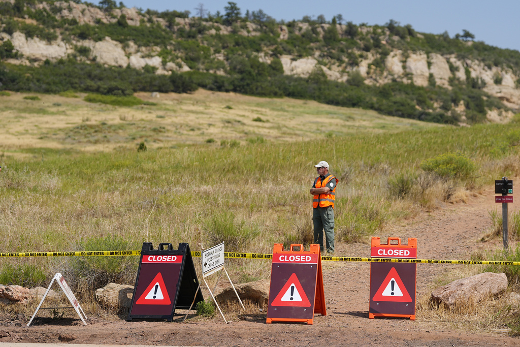 A ranger stands guard along a closed hiking trail as a wildfire burns in neighboring ridges 