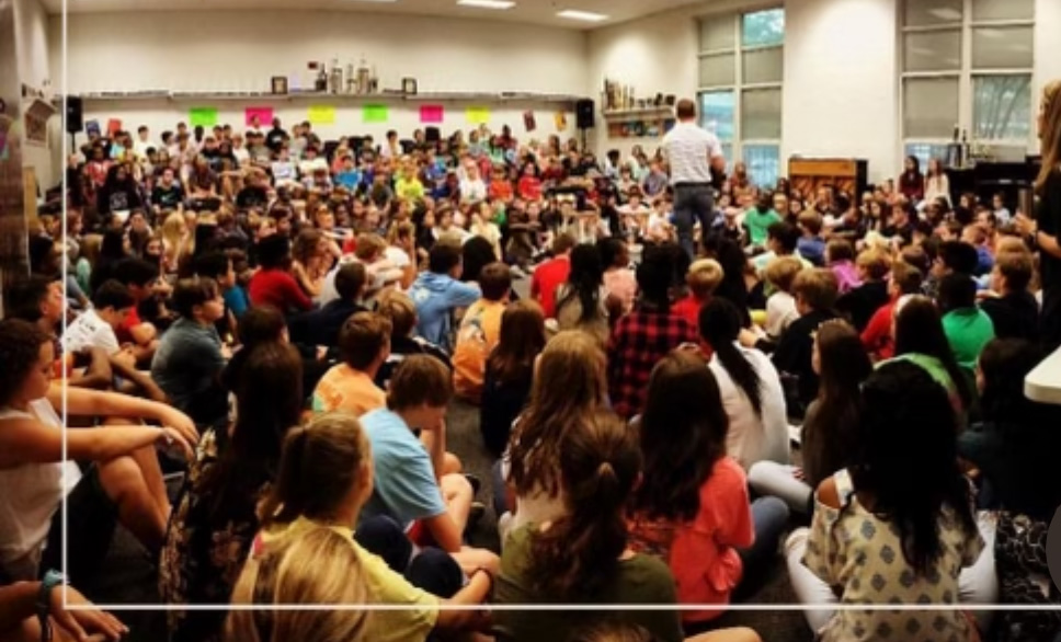 Man in white shirt, standing, surrounded by high school students