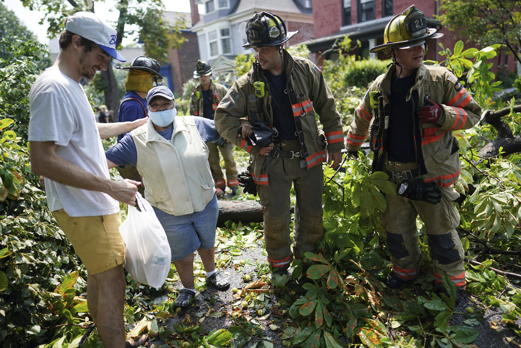 A bystander and firefighters help a woman pass through Prospect Avenue after a sudden storm ripped through the neighborhood in Buffalo, N.Y.