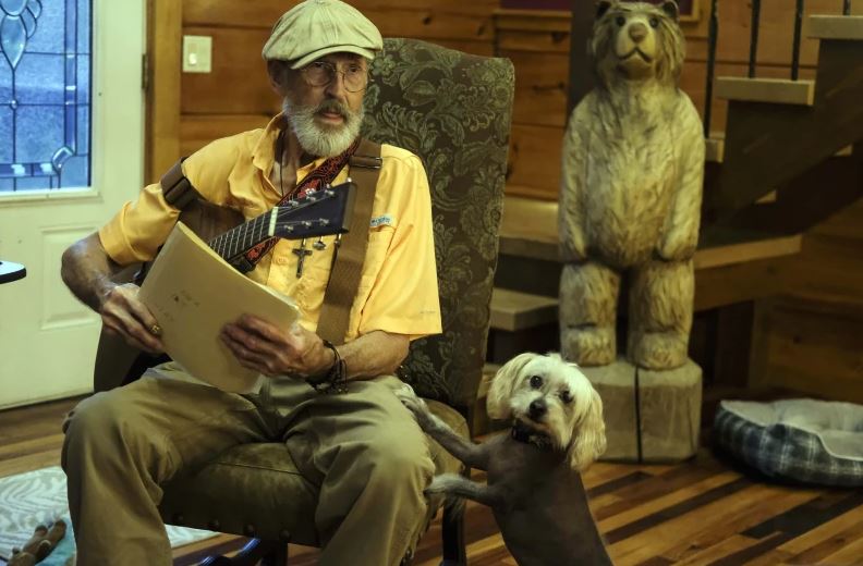 The Rev. Ron Blakely rehearses with sheet music and scripture for his Sunday Gospel Hour at Robert’s Western World honky tonk at his log cabin home near Watertown, Tenn. next to his dog Ope on Friday, July 26, 2024. 