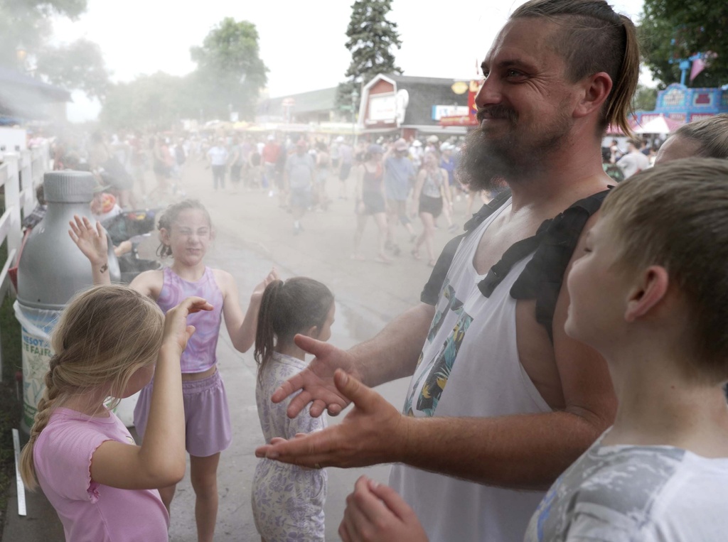 Seven-year-old Harper Perkins, center, and her sister Brielle, of Princeton, Minn., cool off in a misting fountain at the Minnesota State Fair