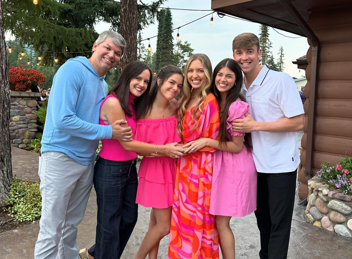 Six people posing for a photo, four women in bright pink dresses and tops