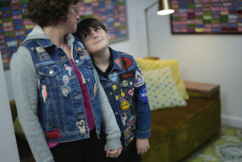 Oliver Burkhardt, 13, looks up at his mom Trisha Brookbank as they hold hands inside the offices of the Oliver Patch Project