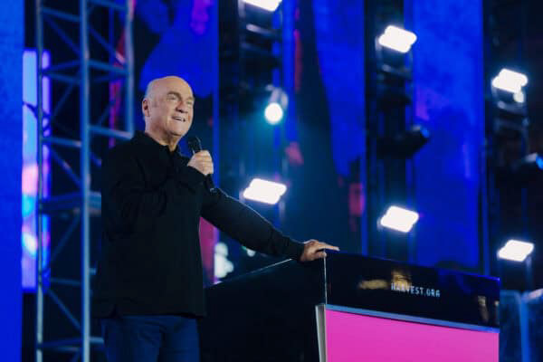 Man on stage with lights behind him and microphone in his hand, smiling