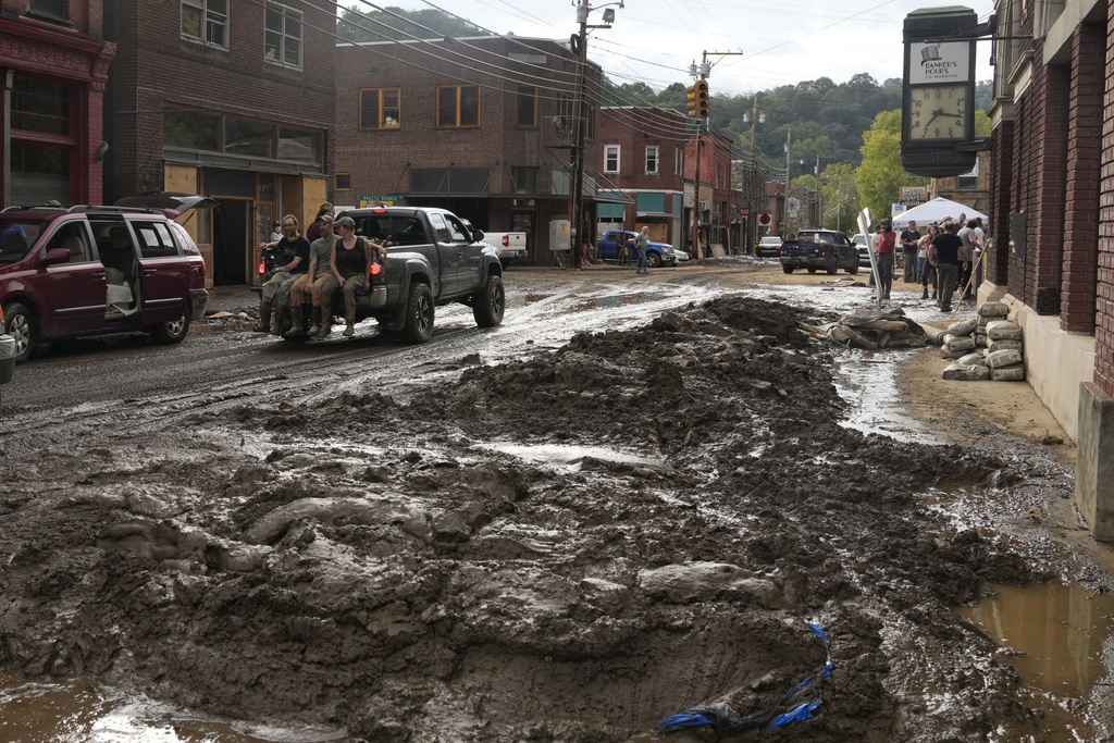 People ride in the back of a pickup truck on a street left covered in deep mud in the aftermath of Hurricane Helene in Marshall, N.C.