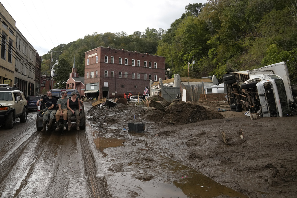 People ride in the back of a pickup truck on a mud-covered street left in the aftermath of Hurricane Helene in Marshall, N.C.