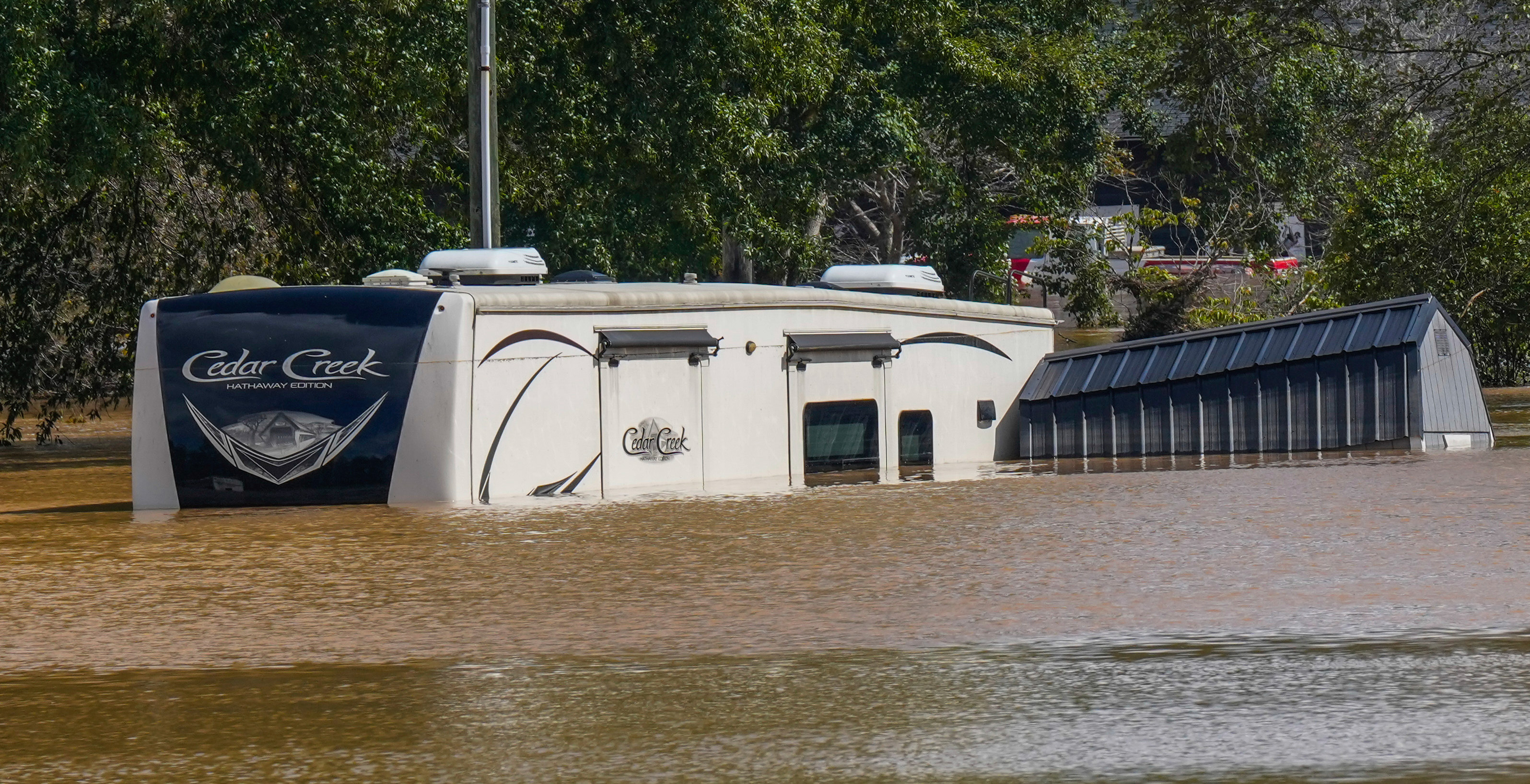 Half of an RV sticking above flood water next to a shed