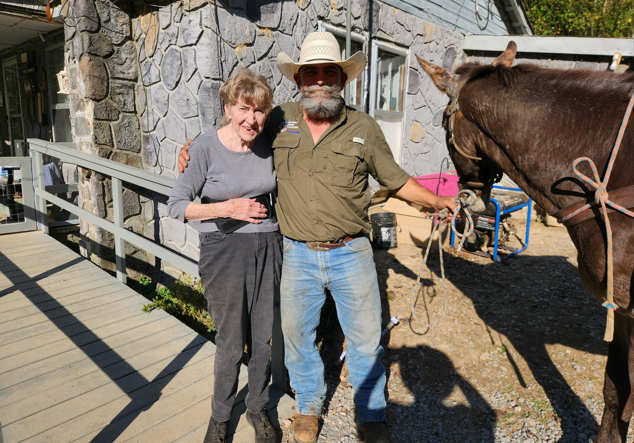 Elderly woman with wrangler and mule in front of her house