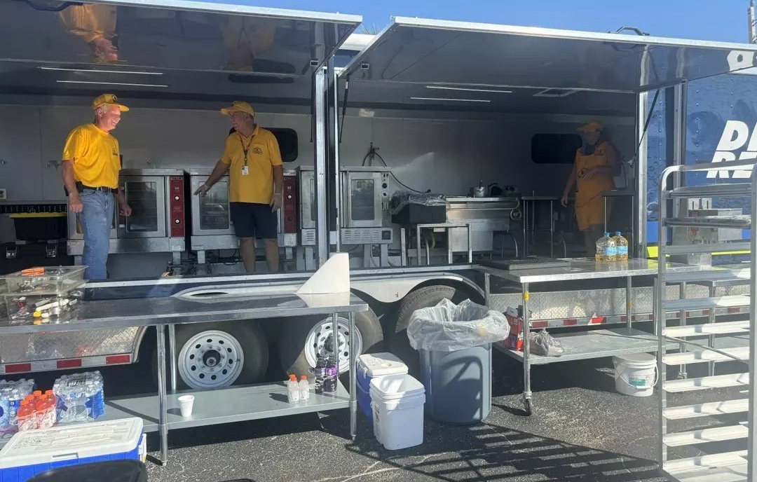 Three people inside of a food ruck with ovens, a sink, etc.