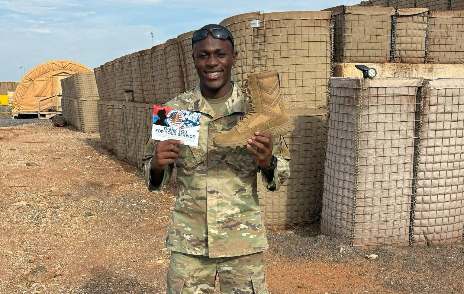 Young soldier in uniform holding up a boot and a thank you for your service card