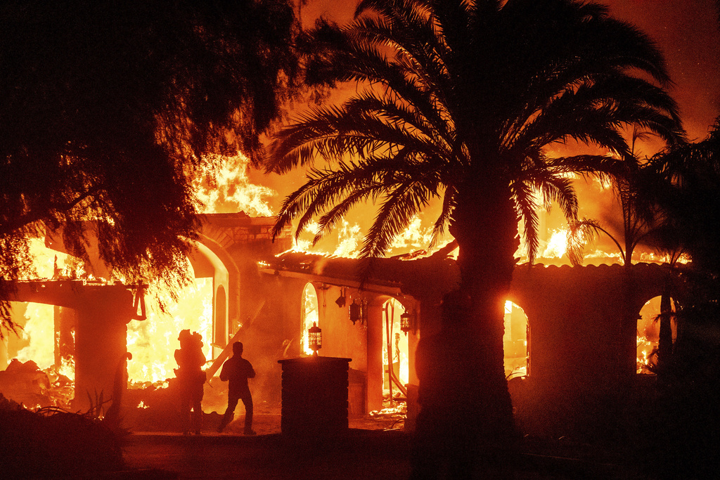 Television reporters film as flames from the Mountain Fire consume a home in Camarillo, Calif.