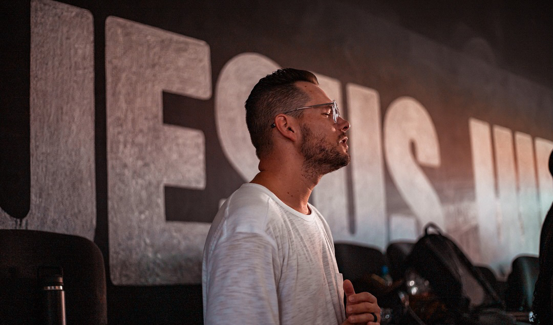 Man worshipping with a huge Jesus sign on the wall behind him