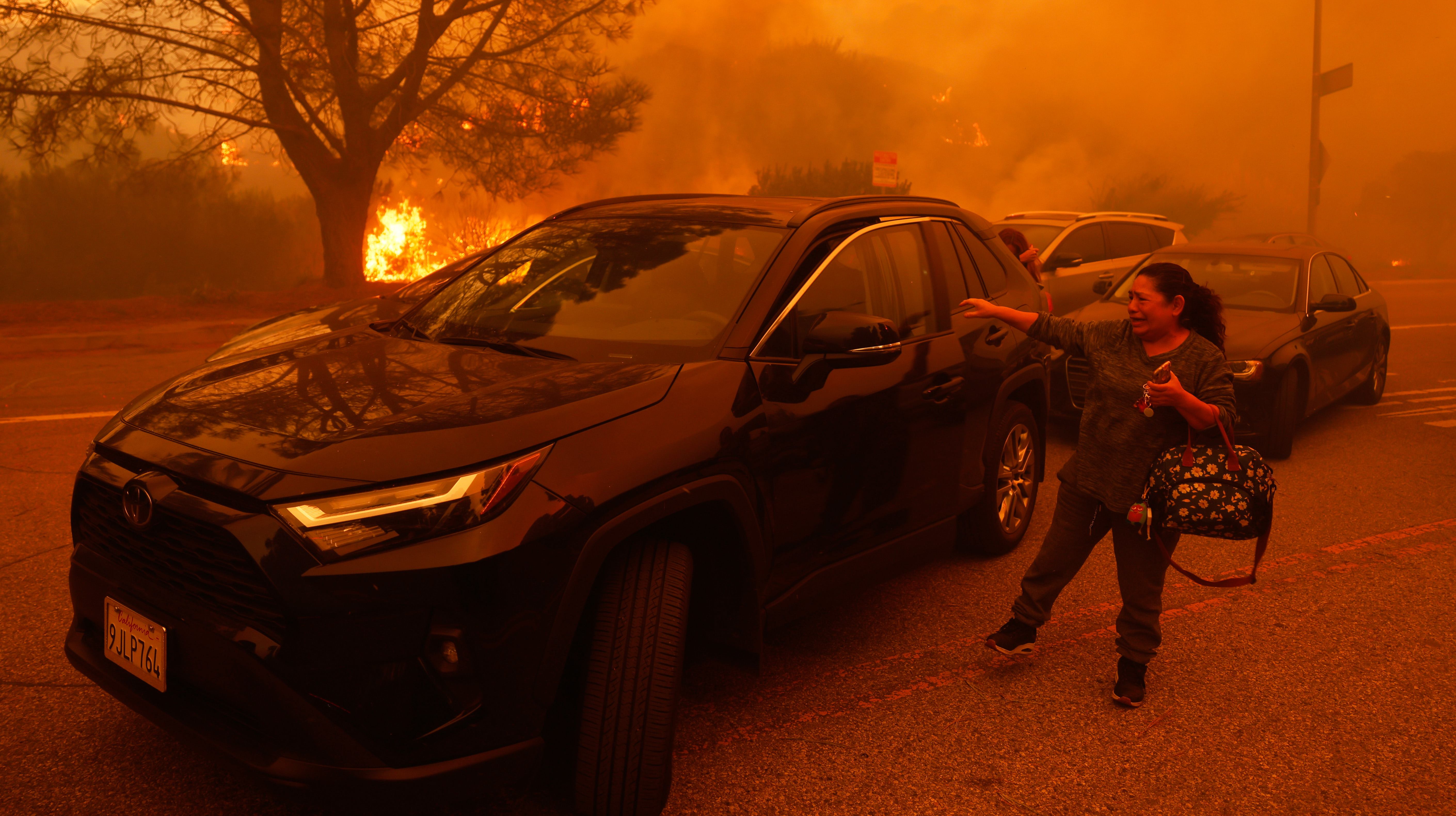 Woman next to car, crying with fire in the background