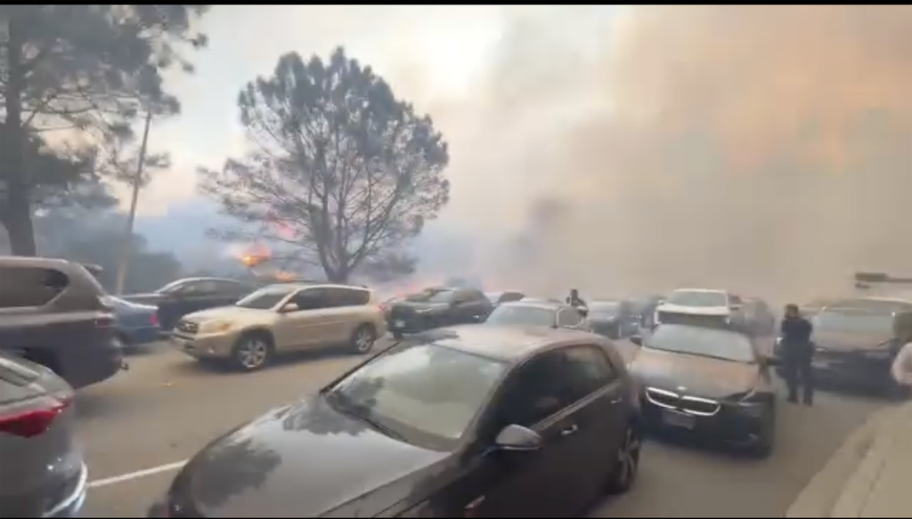 People evacuate their cars as flames from a wildfire spread to the street near Pacific Palisades, Calif.