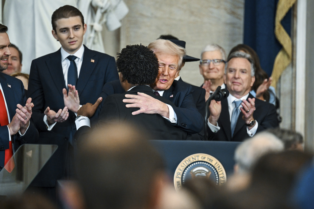 Senior Pastor Lorenzo Sewell, second left, hugs President Donald Trump during the 60th Presidential Inauguration