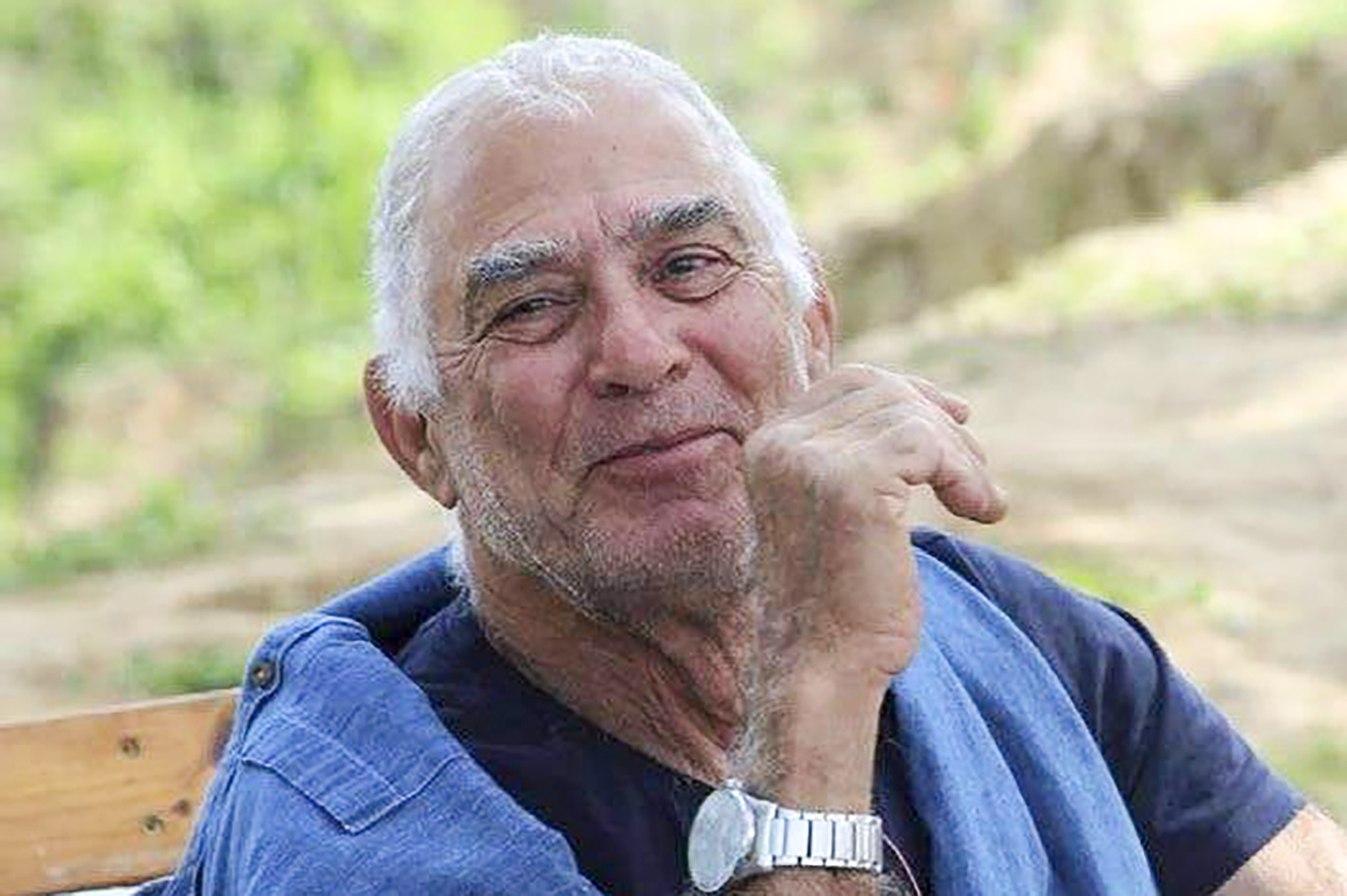 Older man smiling and sitting near a vineyard or a field