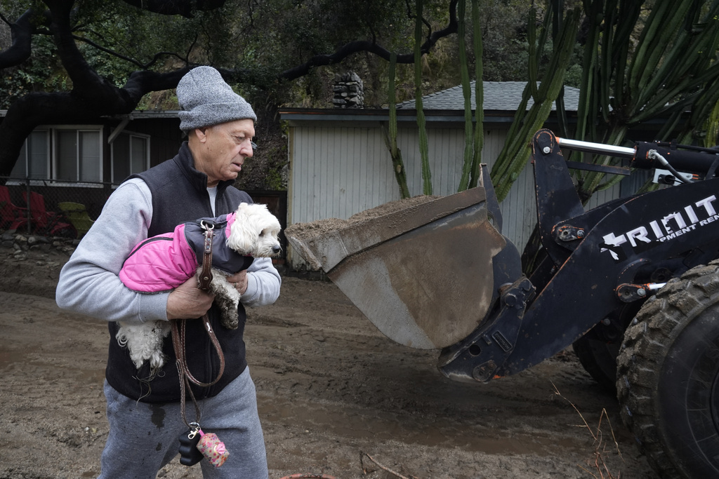 Resident carries their dog past a mud-covered street after a storm in Sierra Madre, Calif. 