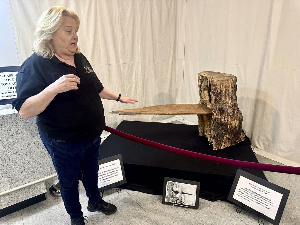 Mary Riseling, coordinator of the commemoration of the 100th anniversary of the March 18 Tri-State Tornado, shows how winds drove a board into the trunk of a maple tree on display at the Jackson County Historical Society