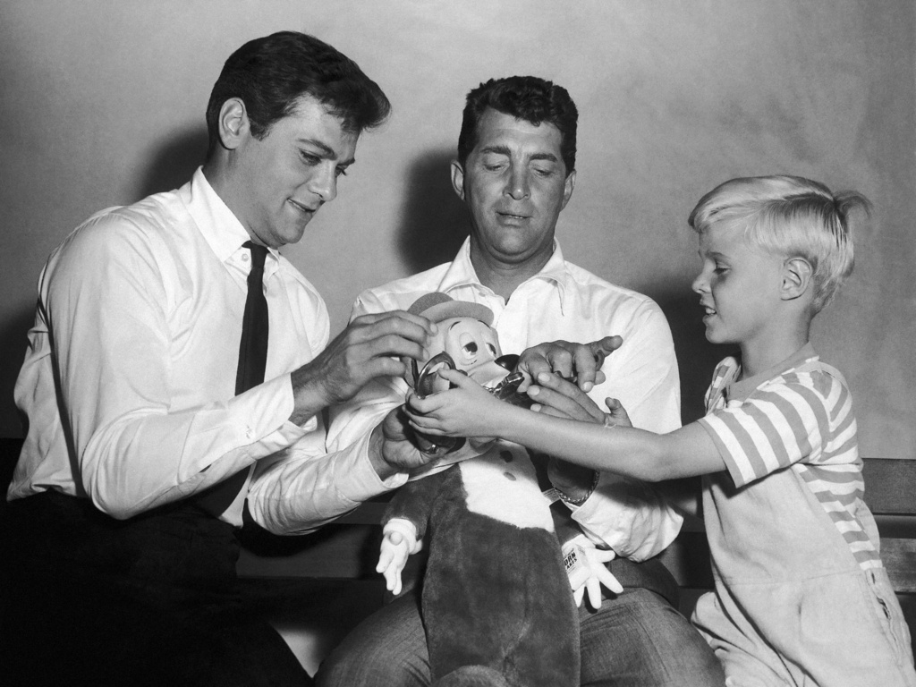 Jay North, young star of the new "Dennis the Menace" series, right, attempts to handcuff Dean Martin, center, as they play with a stuffed toy with Tony Curtis
