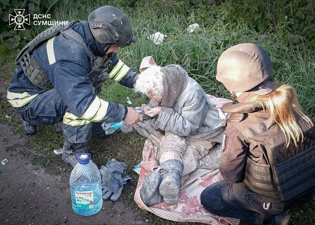 Rescue worker helps an injured elderly woman evacuated from a building which was heavily damaged by a Russian strike in Sumy region