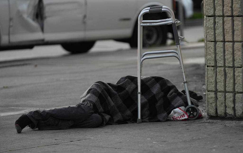 Homeless person sleeps under a light rain on a sidewalk in Los Angeles