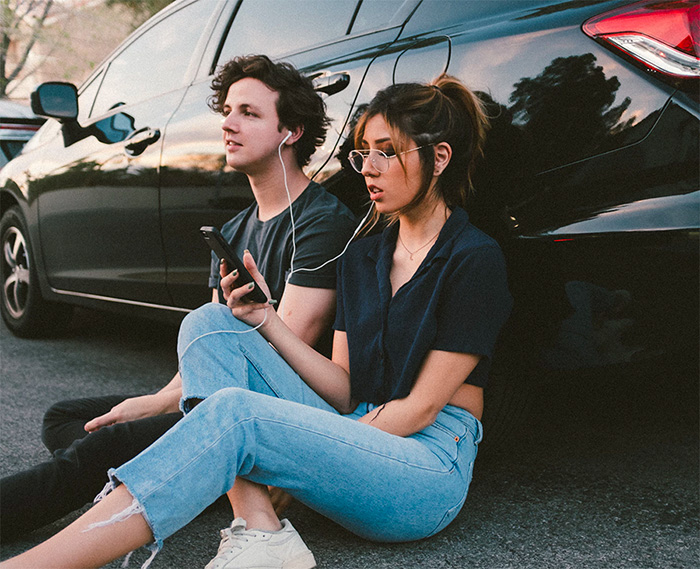 Two people listening to music leaning on a car